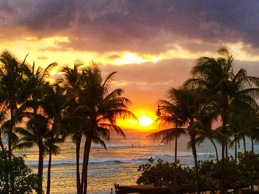 Dramatic sunset at Waikiki Beach with palm trees in the foreground and waves breaking on the shore